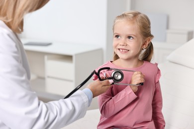 Little girl with stethoscope having fun with doctor in hospital