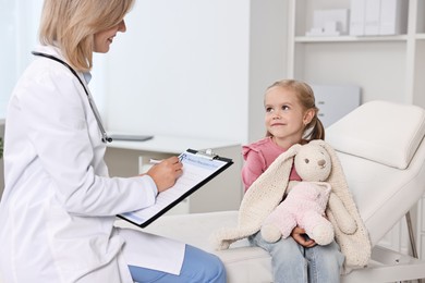 Photo of Doctor consulting little girl with toy in hospital, closeup