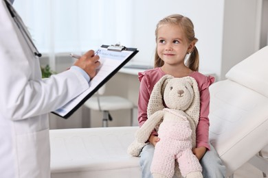 Photo of Doctor consulting little girl with toy in hospital, closeup