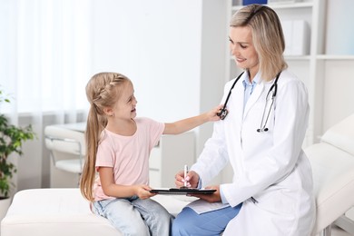 Doctor with clipboard consulting little girl in hospital