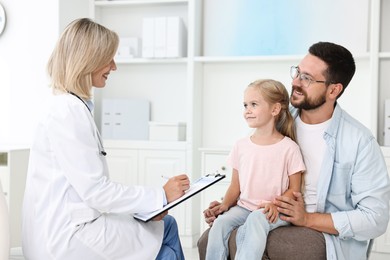 Doctor with clipboard consulting little girl and her father in hospital