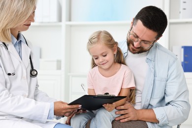 Doctor with clipboard consulting little girl and her father in hospital