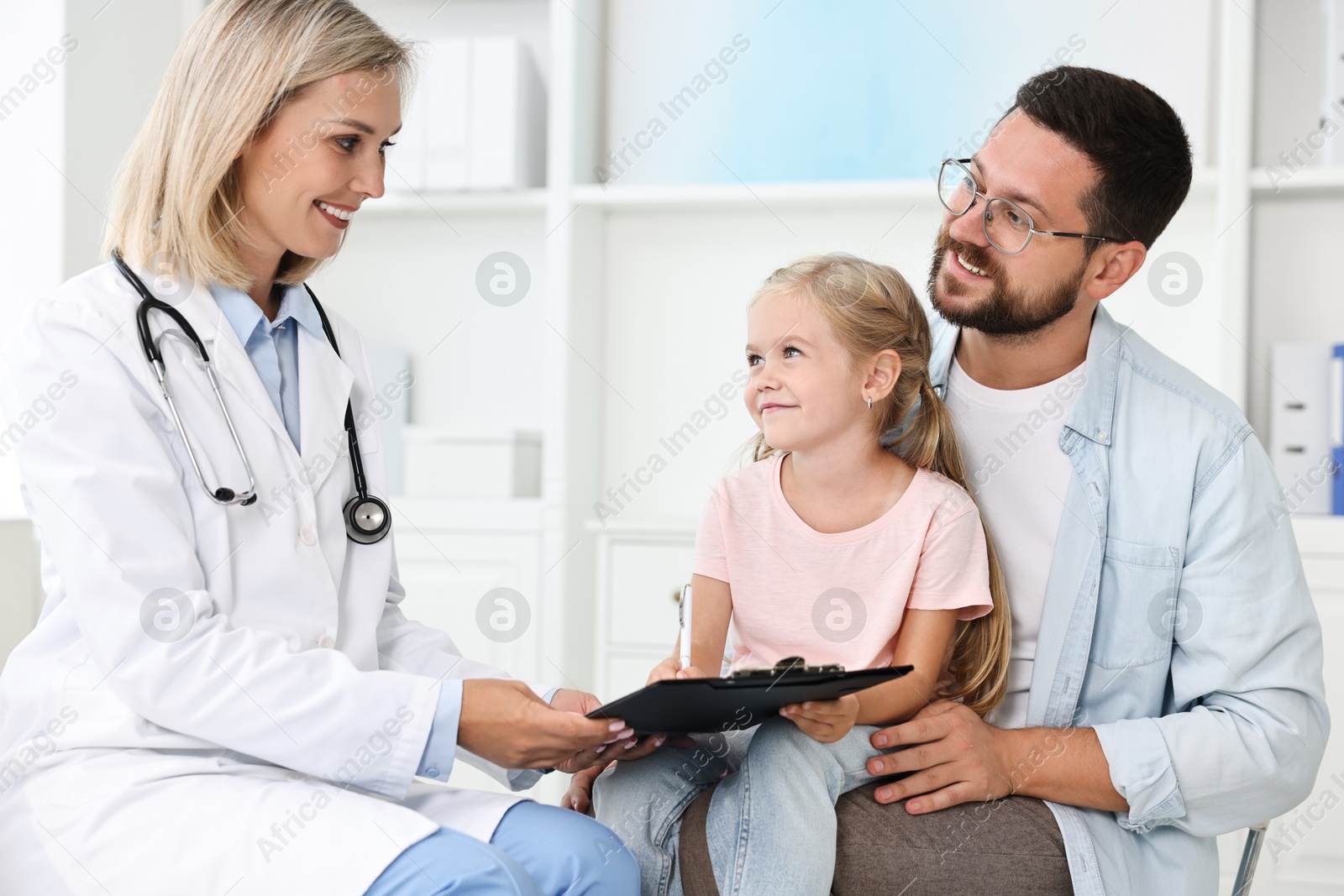 Photo of Doctor with clipboard consulting little girl and her father in hospital