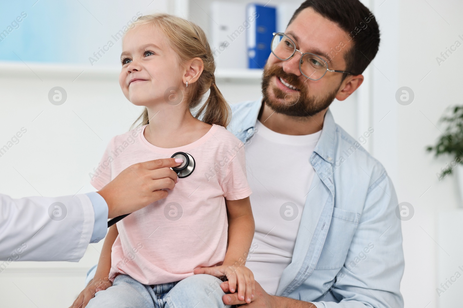 Photo of Doctor examining little girl with stethoscope and her father in hospital, closeup