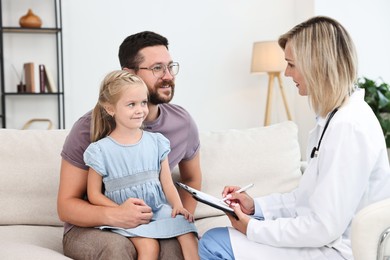 Photo of Doctor with clipboard consulting little girl and her father indoors