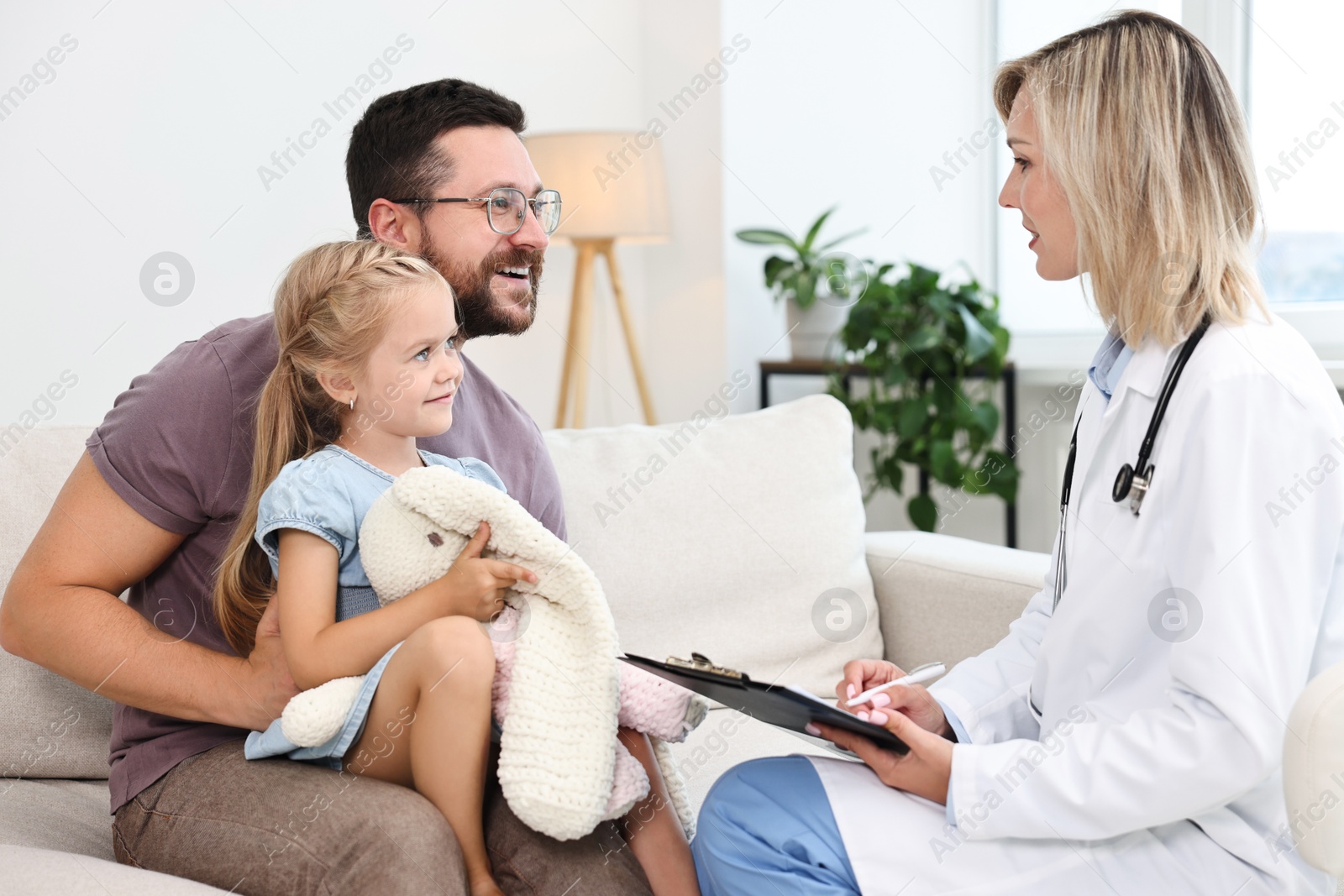 Photo of Doctor consulting little girl with toy and her father indoors