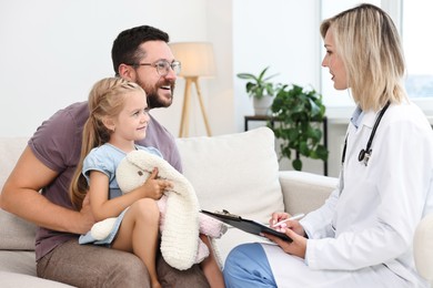 Doctor consulting little girl with toy and her father indoors