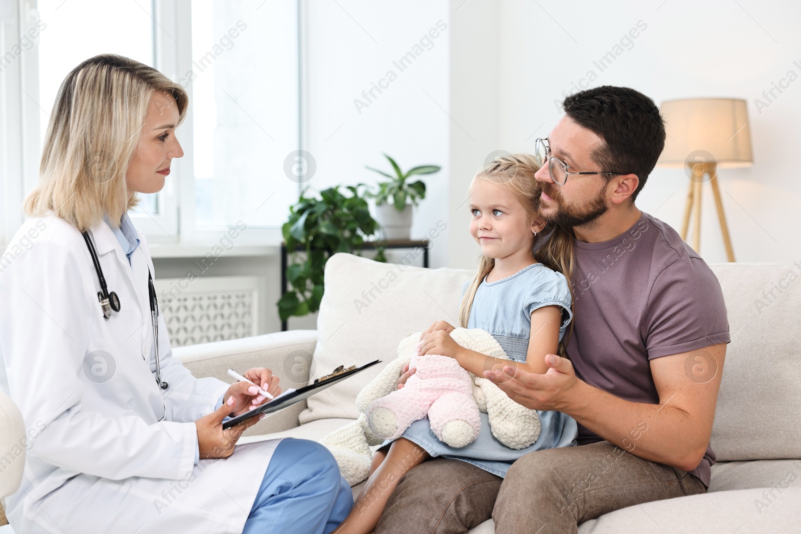 Photo of Doctor consulting little girl with toy and her father indoors