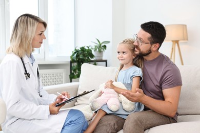 Photo of Doctor consulting little girl with toy and her father indoors