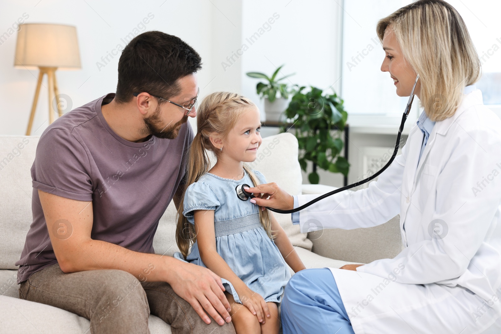 Photo of Doctor examining little girl with stethoscope and her father indoors