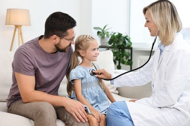 Doctor examining little girl with stethoscope and her father indoors