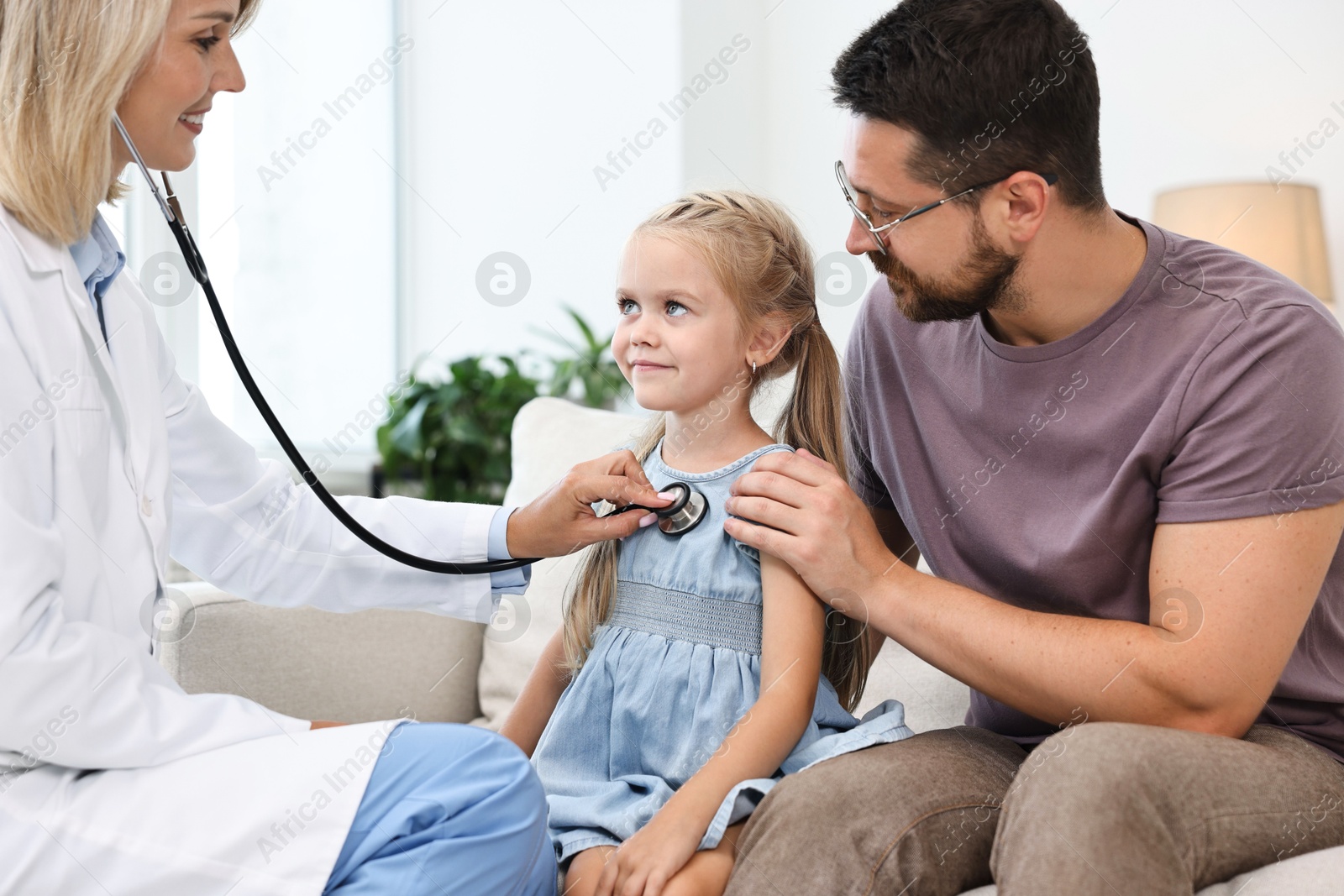 Photo of Doctor examining little girl with stethoscope and her father indoors