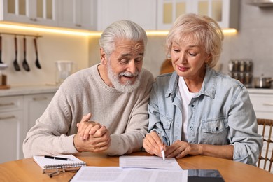 Photo of Pension savings. Senior couple planning budget at wooden table indoors