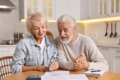 Pension savings. Senior couple planning budget at wooden table indoors