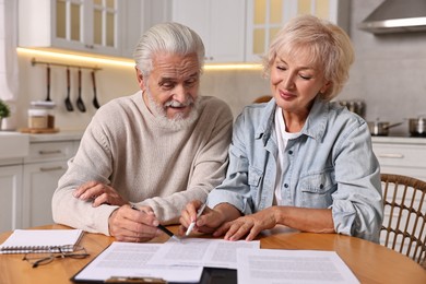 Photo of Pension savings. Senior couple planning budget at wooden table indoors