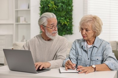 Photo of Pension savings. Senior couple planning budget at white table indoors