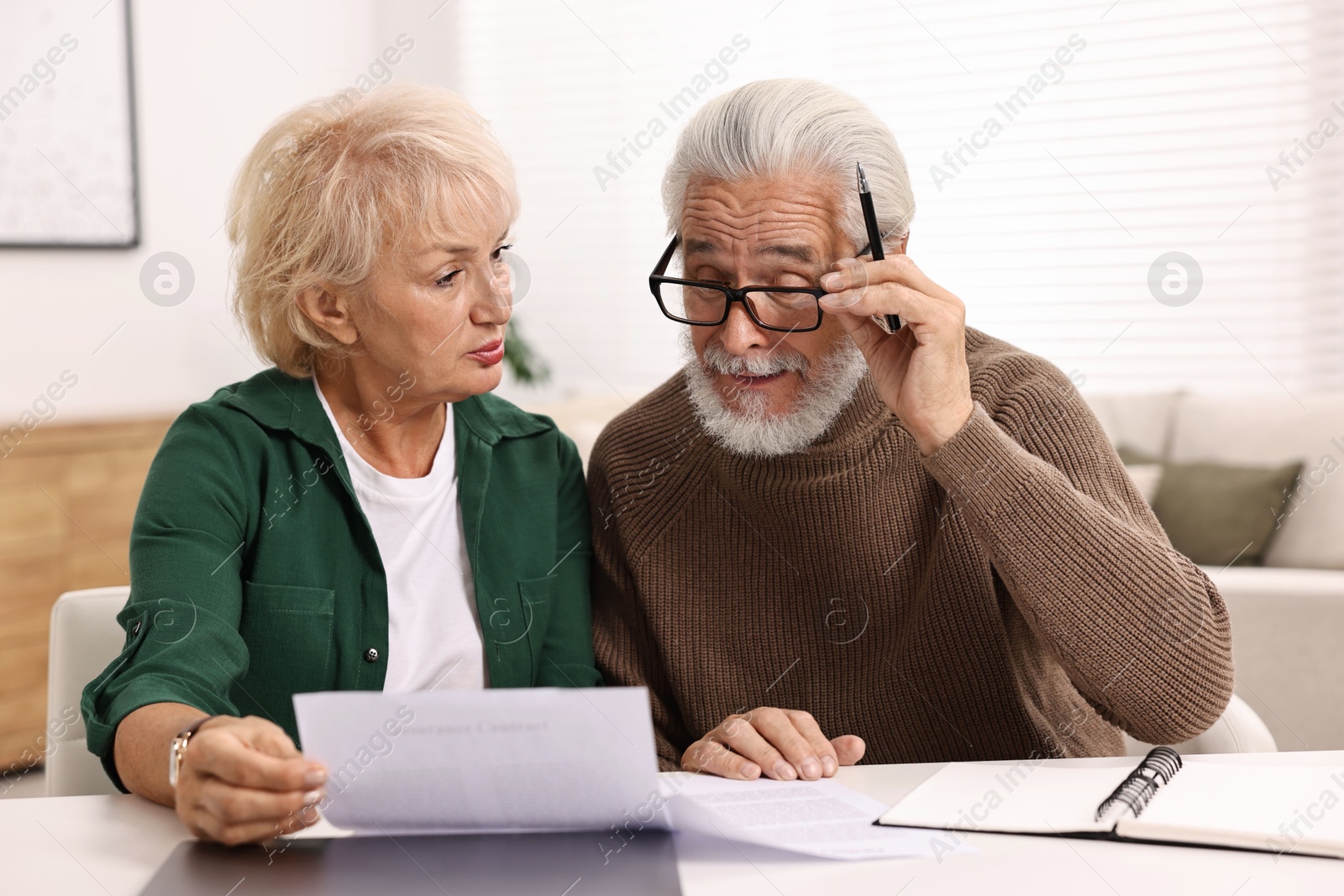 Photo of Pension savings. Senior couple planning budget at white table indoors