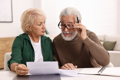 Photo of Pension savings. Senior couple planning budget at white table indoors