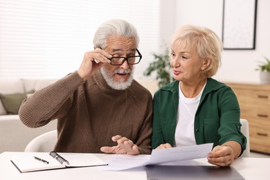 Photo of Pension savings. Senior couple planning budget at white table indoors