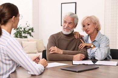 Pension plan. Senior couple consulting with insurance agent at wooden table indoors