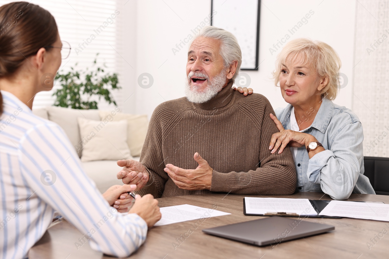 Photo of Pension plan. Senior couple consulting with insurance agent at wooden table indoors