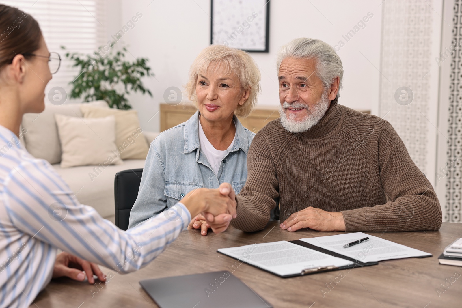 Photo of Pension plan. Senior couple consulting with insurance agent at wooden table indoors