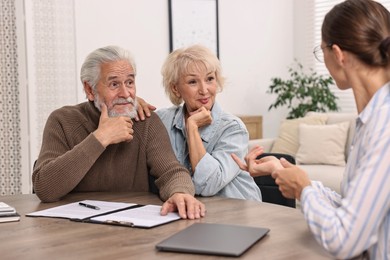 Pension plan. Senior couple consulting with insurance agent at wooden table indoors