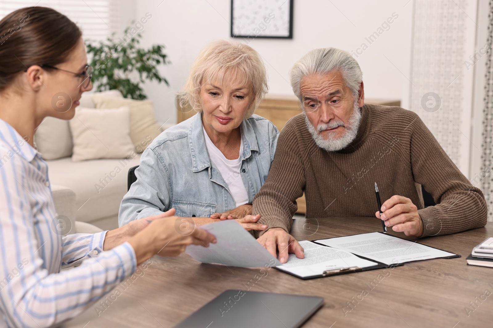 Photo of Pension plan. Senior couple consulting with insurance agent at wooden table indoors