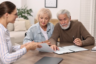 Pension plan. Senior couple consulting with insurance agent at wooden table indoors