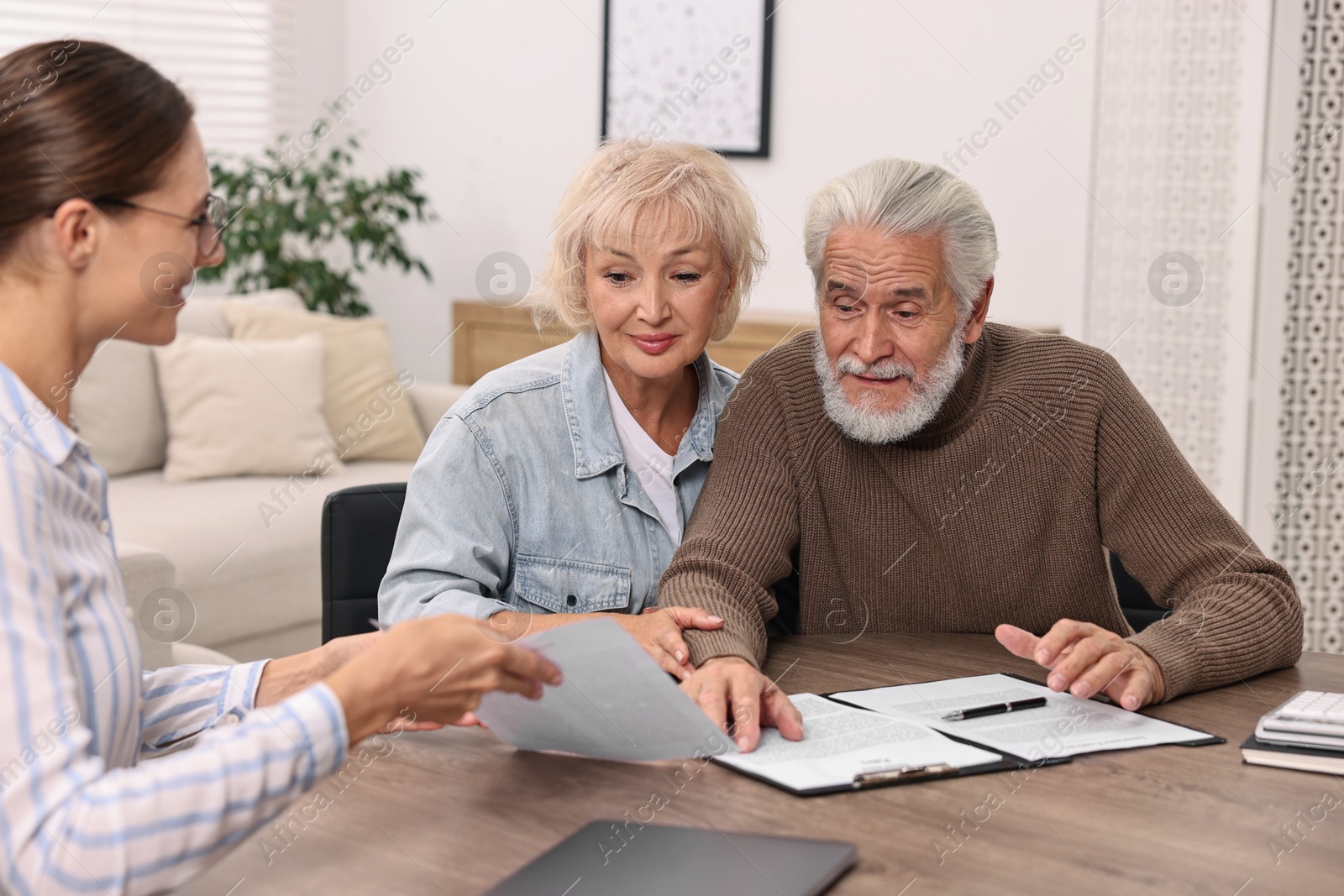 Photo of Pension plan. Senior couple consulting with insurance agent at wooden table indoors