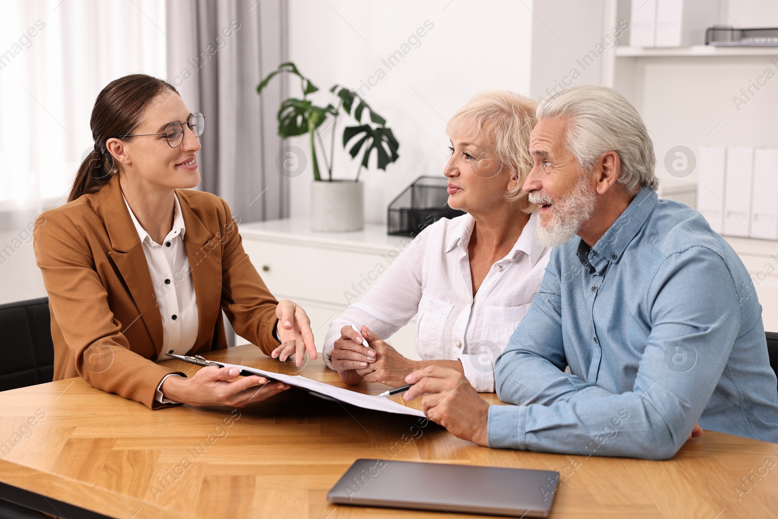 Photo of Pension plan. Senior couple consulting with insurance agent at wooden table indoors