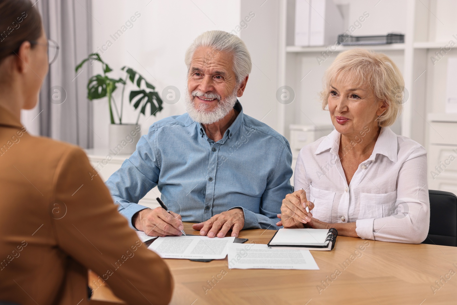 Photo of Pension plan. Senior couple consulting with insurance agent at wooden table indoors