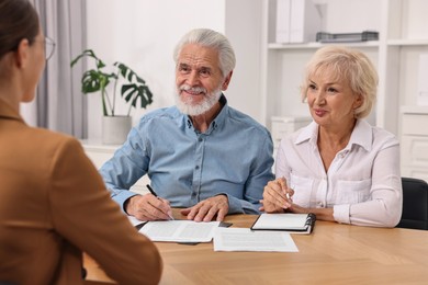 Photo of Pension plan. Senior couple consulting with insurance agent at wooden table indoors