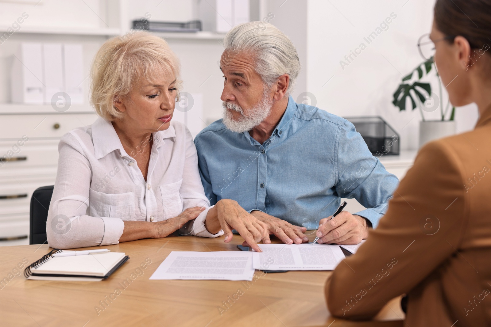 Photo of Pension plan. Senior couple consulting with insurance agent at wooden table indoors