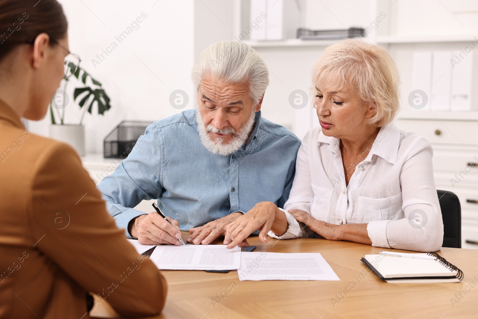 Photo of Pension plan. Senior couple consulting with insurance agent at wooden table indoors