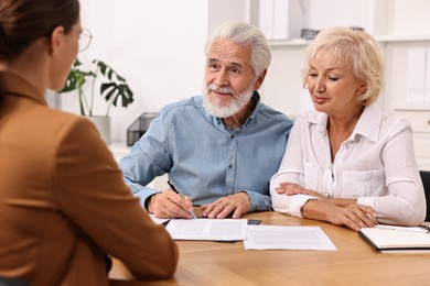 Photo of Pension plan. Senior couple consulting with insurance agent at wooden table indoors