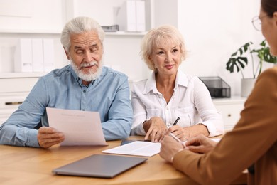 Pension plan. Senior couple consulting with insurance agent at wooden table indoors