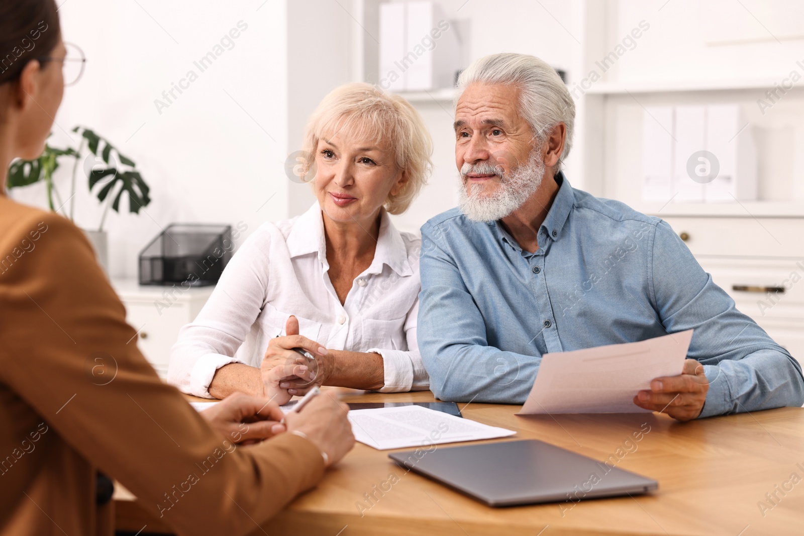 Photo of Pension plan. Senior couple consulting with insurance agent at wooden table indoors