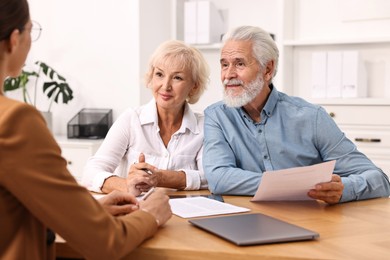 Photo of Pension plan. Senior couple consulting with insurance agent at wooden table indoors