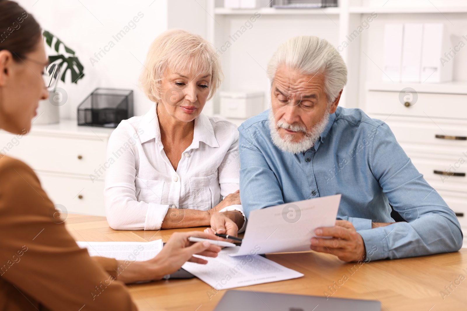 Photo of Pension plan. Senior couple consulting with insurance agent at wooden table indoors