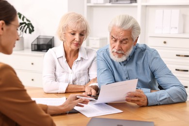 Pension plan. Senior couple consulting with insurance agent at wooden table indoors