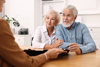 Pension plan. Senior couple consulting with insurance agent at wooden table indoors