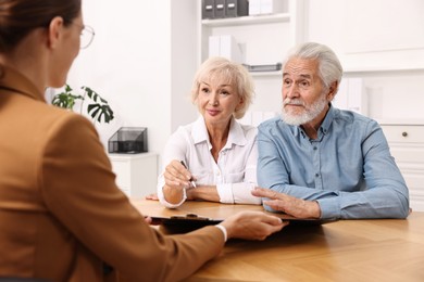 Pension plan. Senior couple consulting with insurance agent at wooden table indoors