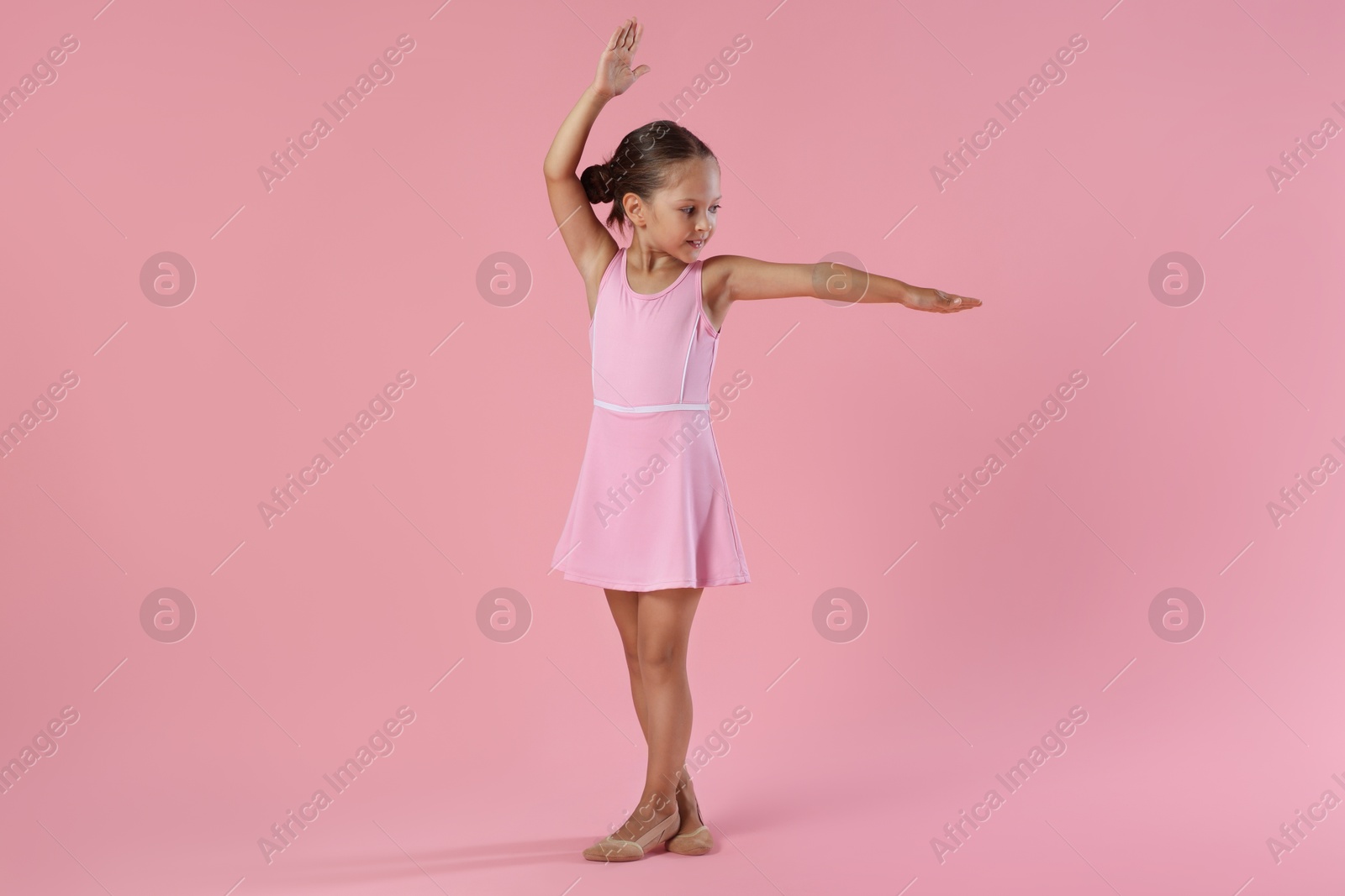 Photo of Little ballerina practicing dance moves on pink background