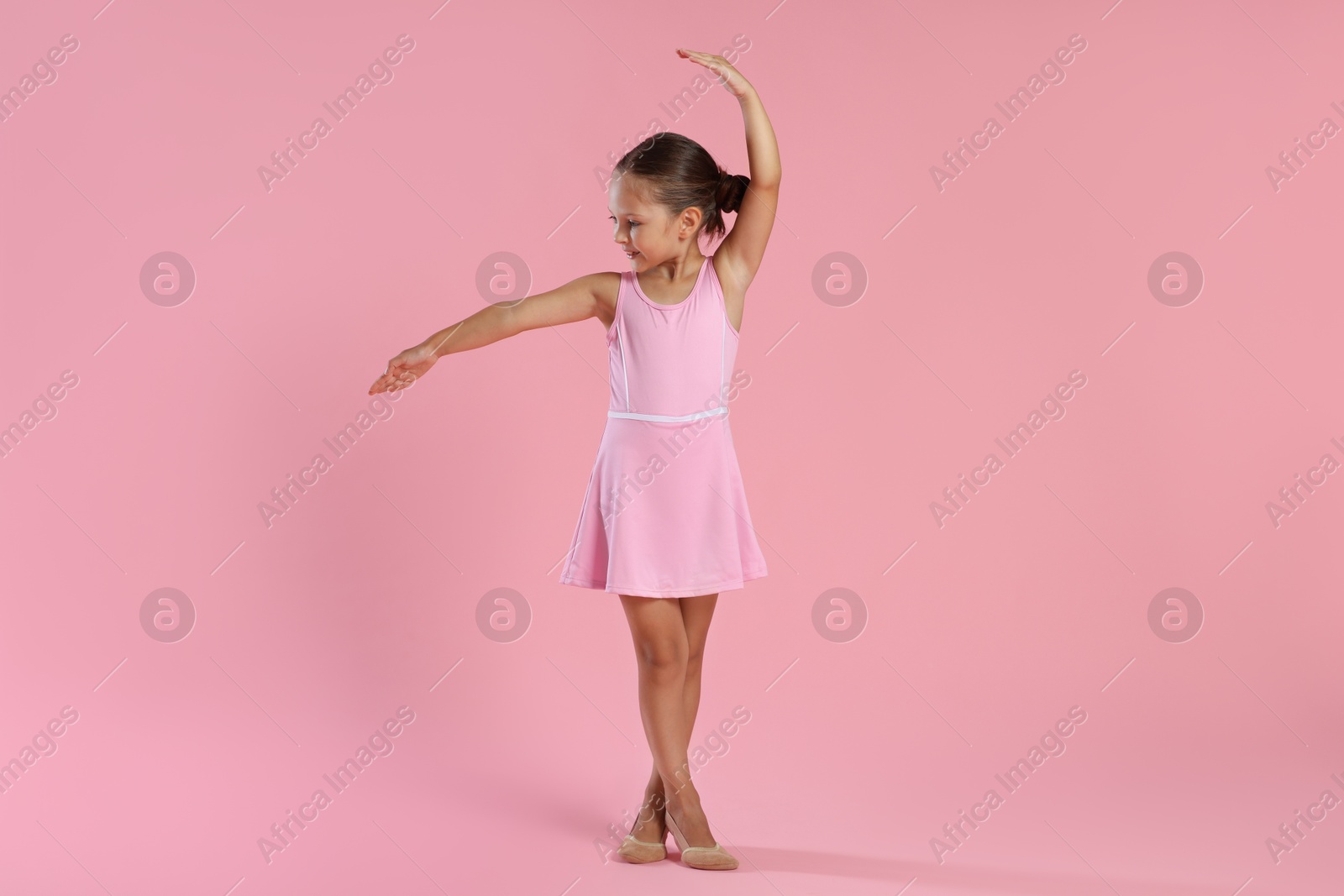 Photo of Little ballerina practicing dance moves on pink background