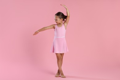 Little ballerina practicing dance moves on pink background