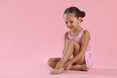 Little ballerina putting on pointe shoes against pink background, space for text