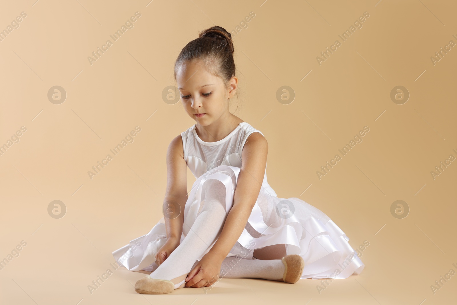 Photo of Little ballerina putting on pointe shoes against beige background