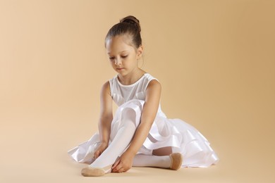 Photo of Little ballerina putting on pointe shoes against beige background