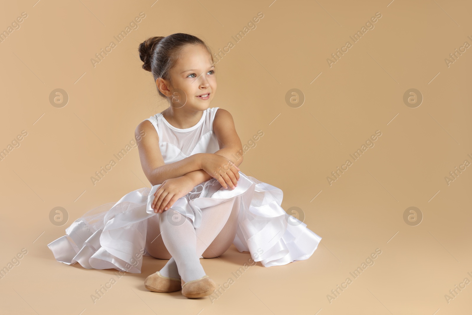 Photo of Portrait of little ballerina on beige background, space for text